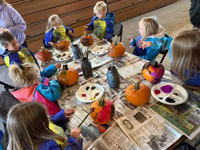 Children painting pumpkins together around a classroom table